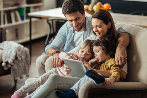 Familie sietzt auf der Couch und steuert per Tablet die Smart-Home-Funktionen